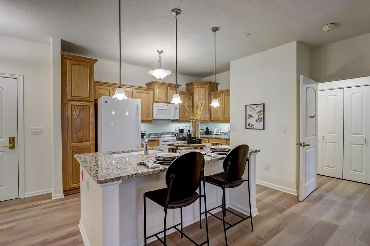 open-concept kitchen featuring a marbled island with hanging pendant lights in an apartment at Newcastle Place Senior Living Community
