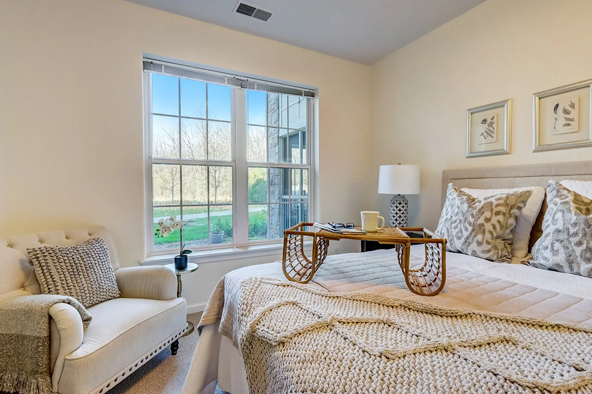 cozy, fully-furnished bedroom with chair in a senior living apartment at Newcastle Place Senior Living Community