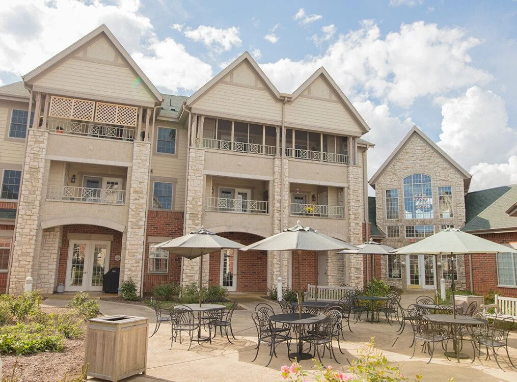 courtyard and outdoor dining space with umbrella tables outside of the charming buildings at Newcastle Place Senior Living Community