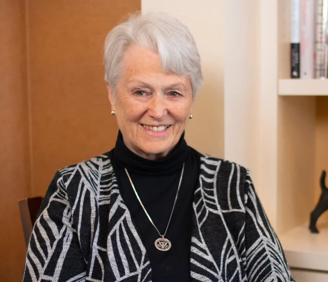 smiling, stylish senior woman, Connie Pukaite, sits in front of a bookshelf for an interview at Newcastle Place
