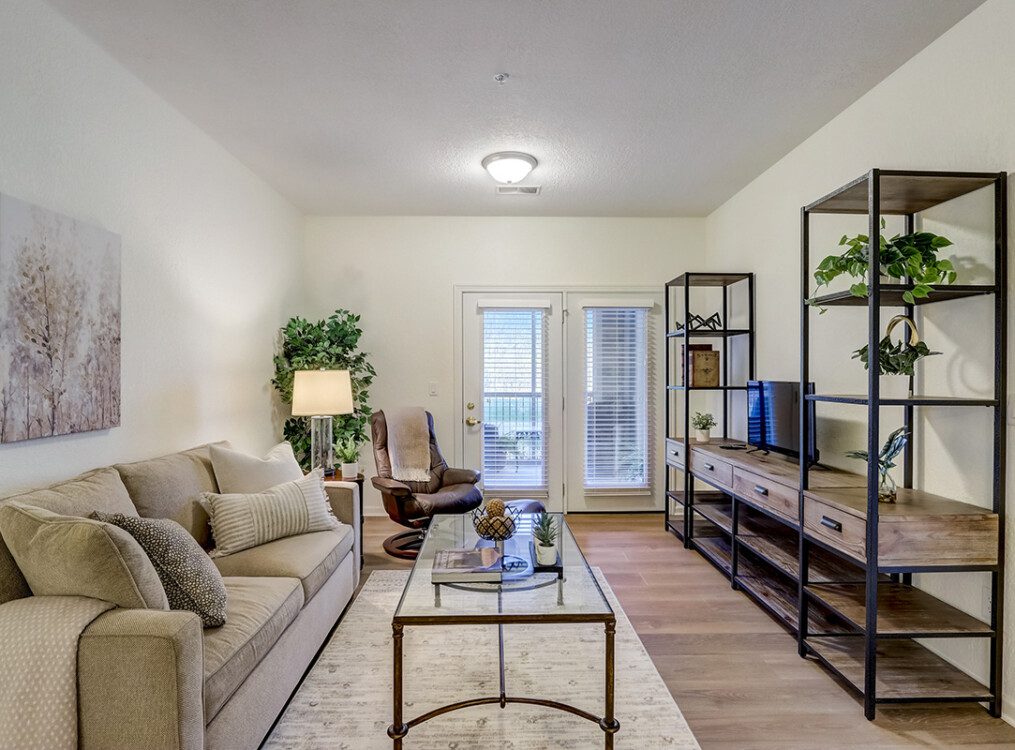 spacious, fully-furnished living room area with view of adjacent patio entryway in an apartment at Newcastle Place Senior Living Community