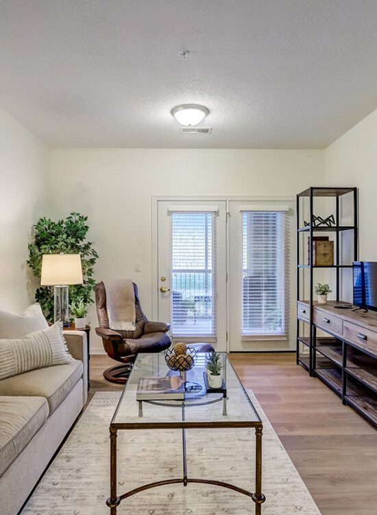 spacious, fully-furnished living room area with view of adjacent patio entryway in an apartment at Newcastle Place Senior Living Community