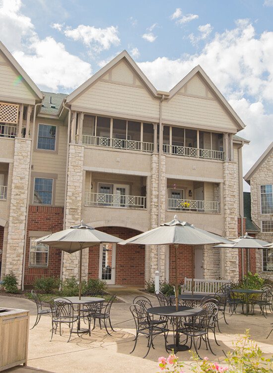 courtyard and outdoor dining space with umbrella tables outside of the charming buildings at Newcastle Place Senior Living Community