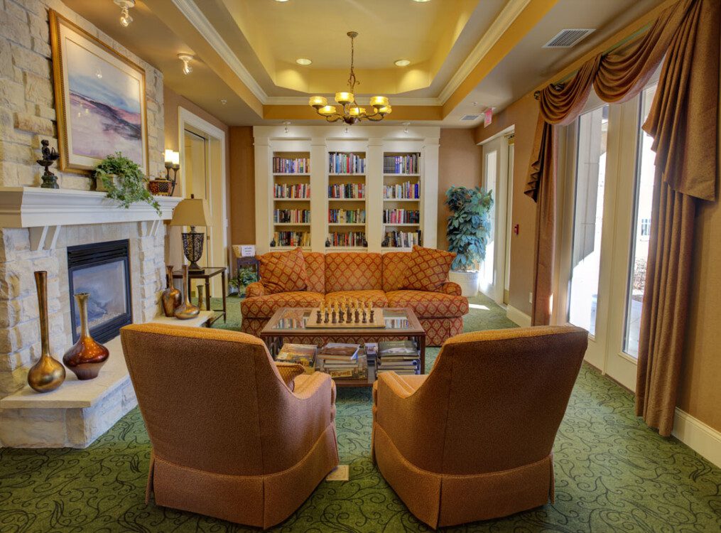 elegant community sitting room with fireplace, cozy seating, and bookshelves at Newcastle Place Senior Living Community