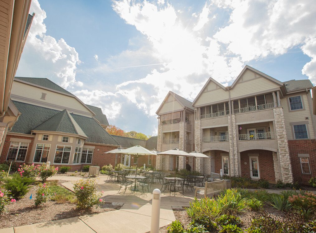 courtyard and outdoor dining space with umbrella tables outside of the charming buildings at Newcastle Place Senior Living Community
