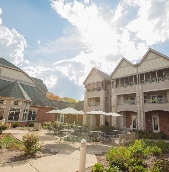 courtyard and outdoor dining space with umbrella tables outside of the charming buildings at Newcastle Place Senior Living Community