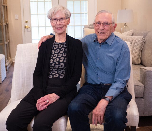 smiling senior couple sit side-by-side in chairs for an interview at Newcastle Place Senior Living Community