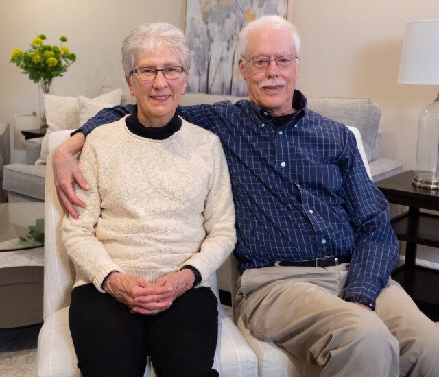 smiling senior couple sits together facing the camera for an interview at Newcastle Place Senior Living Community