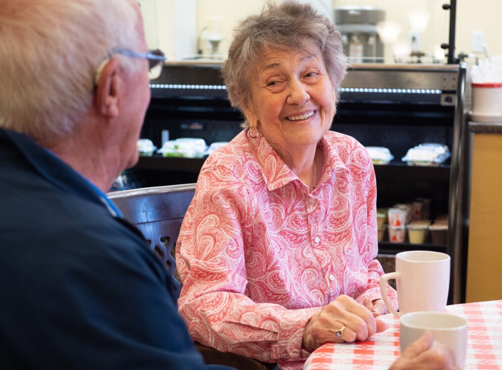 close-up of senior woman smiling at her husband while enjoying coffee at a table in the Castle Cafe at Newcastle Place