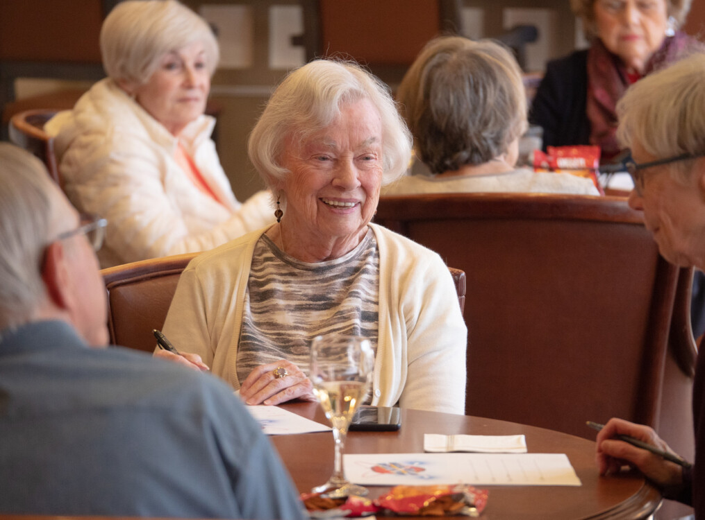 multiple tables of senior friends enjoy snacks and wine during a game night event at Newcastle Place Senior Living Community