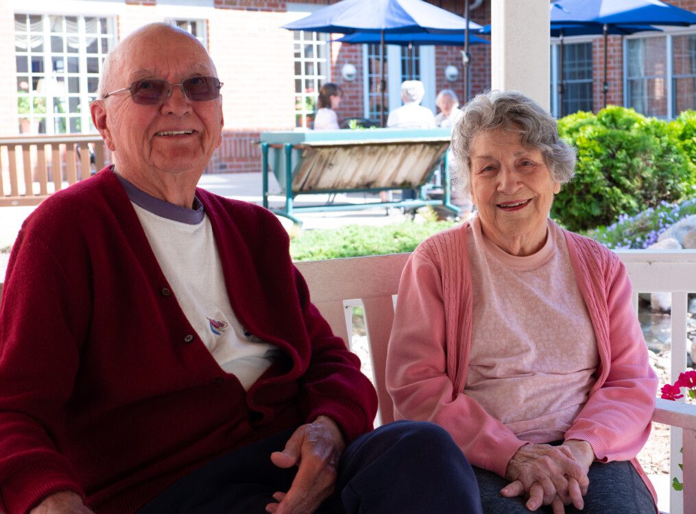 smiling senior couple sits on a bench outdoors at Newcastle Place Senior Living Community