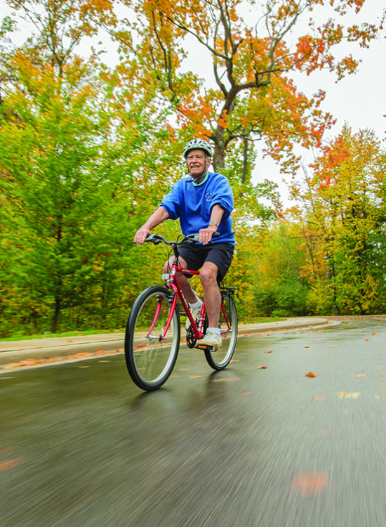 smiling senior man in athletic gear and helmet rides bicycle along a tree-lined road in autumn